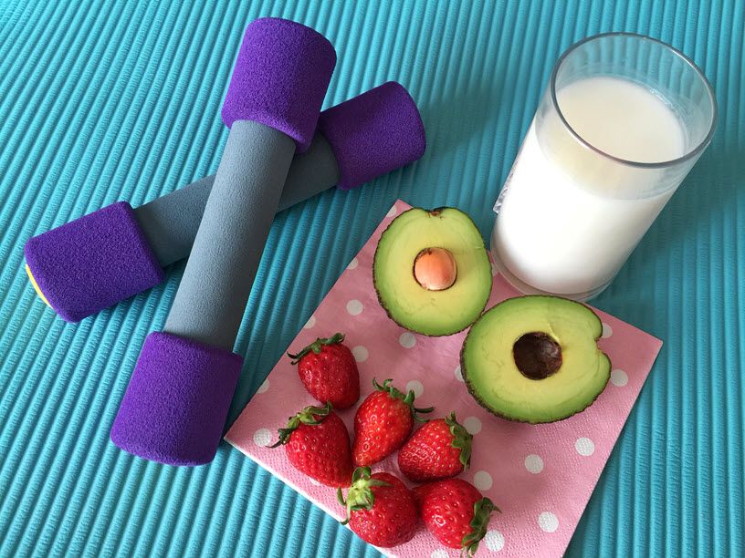 Yoga mat with dumb bells, milk, avocados and strawberries