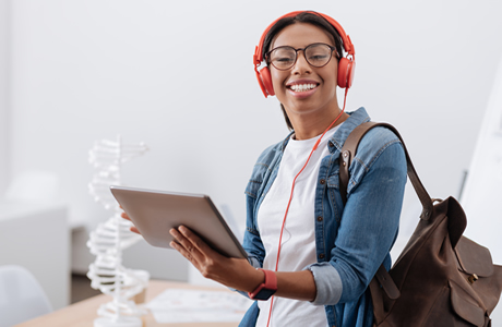 Happy young African-American woman with backpack, holding a tablet and wearing earphones.